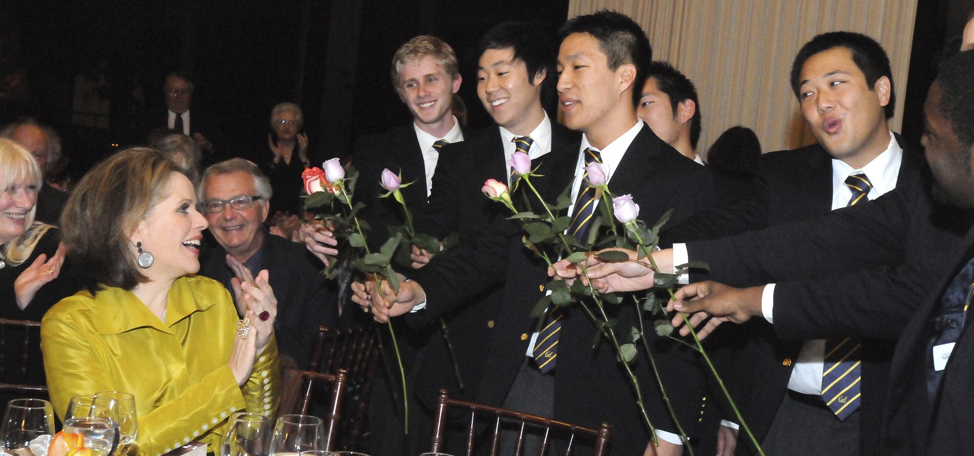 Students handing flowers to woman at table