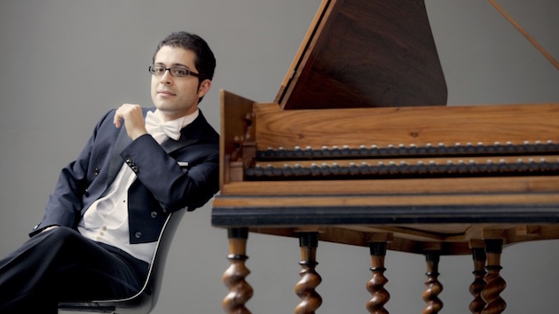 Mahan Esfahani in a tuxedo leans against a harpsichord