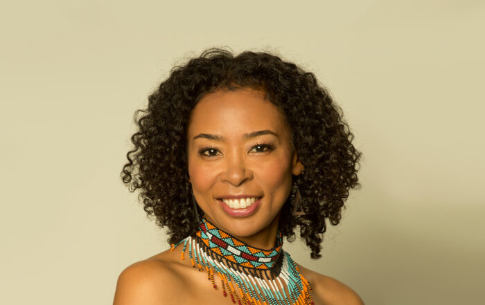 Photo of Nokuthula Ngwenyama, a young Ndebele and Japanese violinist with short curly brown hair. She wears a vibrant beaded collar-like necklace while smiling.