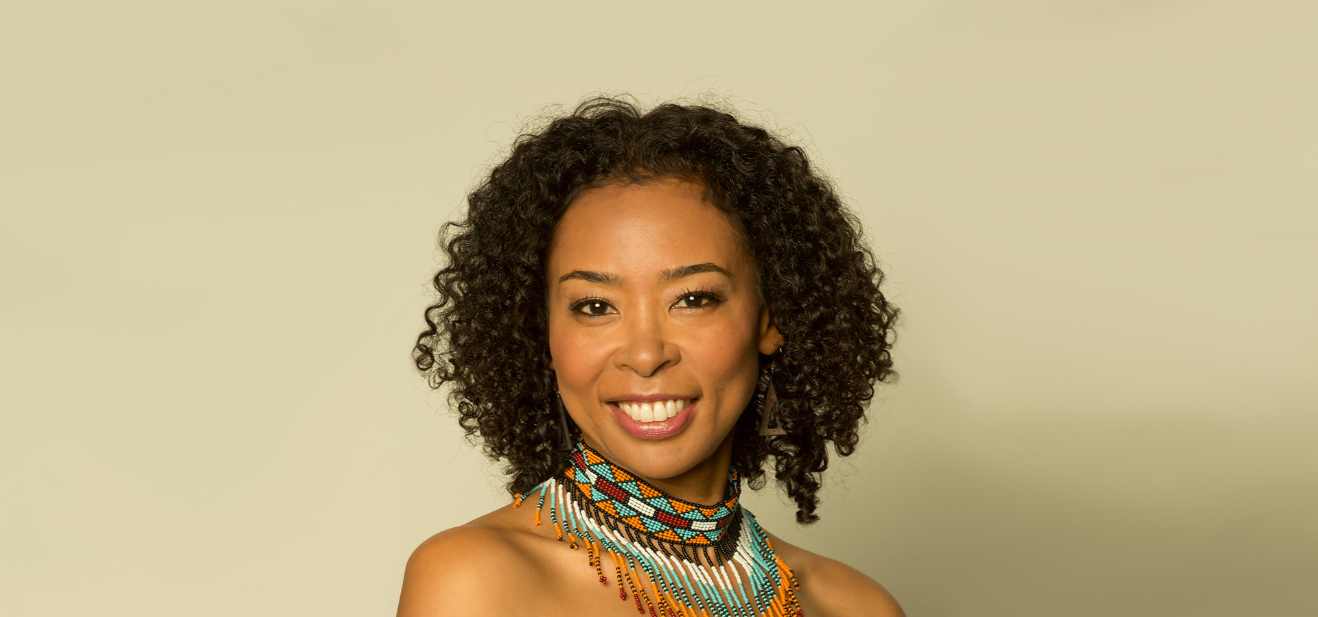 Photo of Nokuthula Ngwenyama, a young Ndebele and Japanese violinist with short curly brown hair. She wears a vibrant beaded collar-like necklace while smiling.