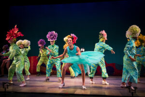 Dorrance Dance performers wear blue and green costumes with large flower shaped headpieces.