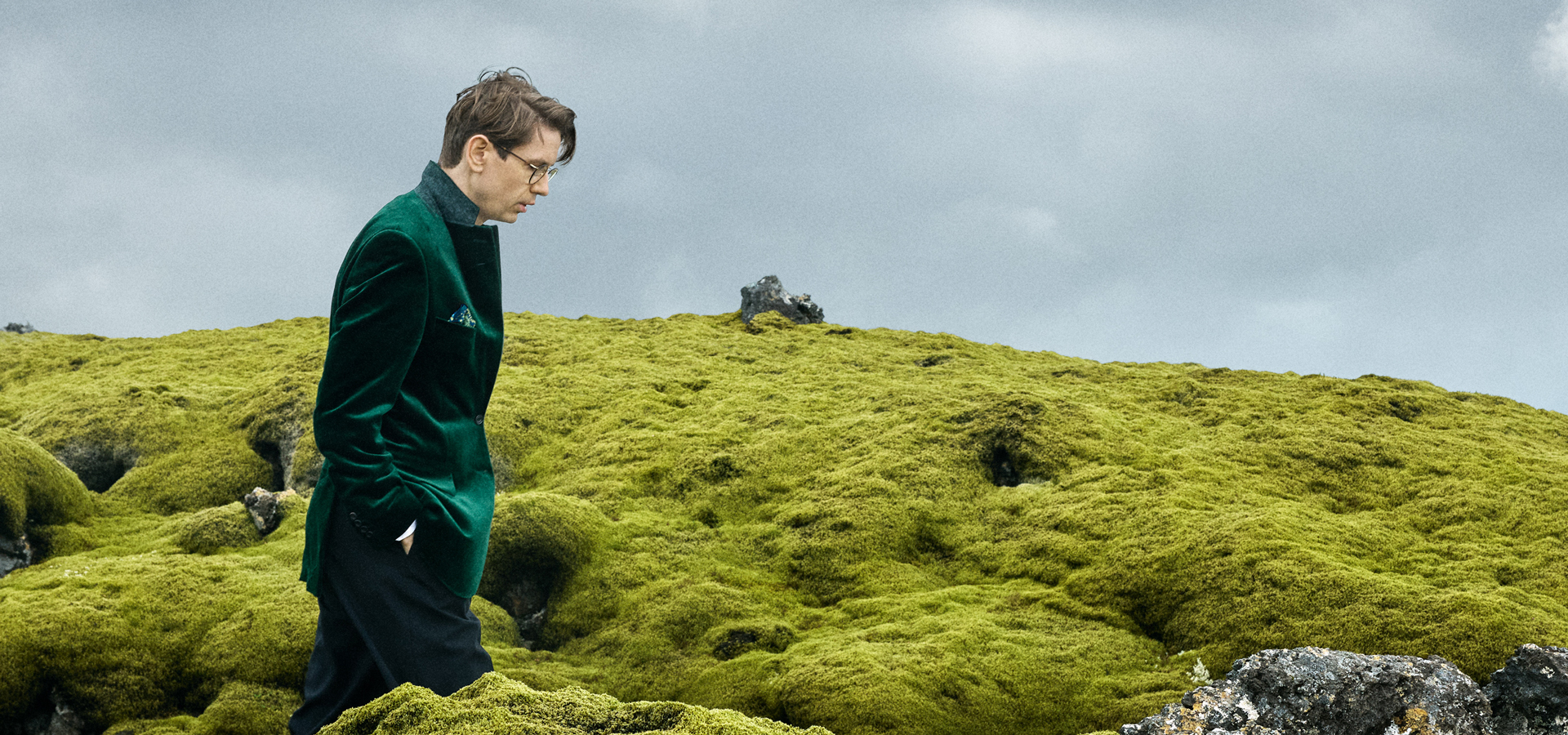 Man with hands in pockets walking through green field
