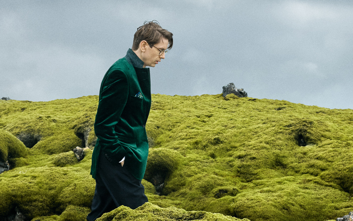 Man with hands in pockets walking through green field