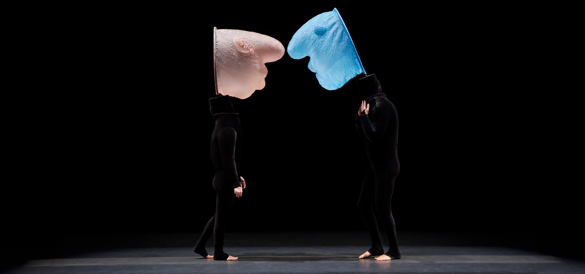 Performers in all-black outfits dance with abstract inflatable heads attached to their heads.