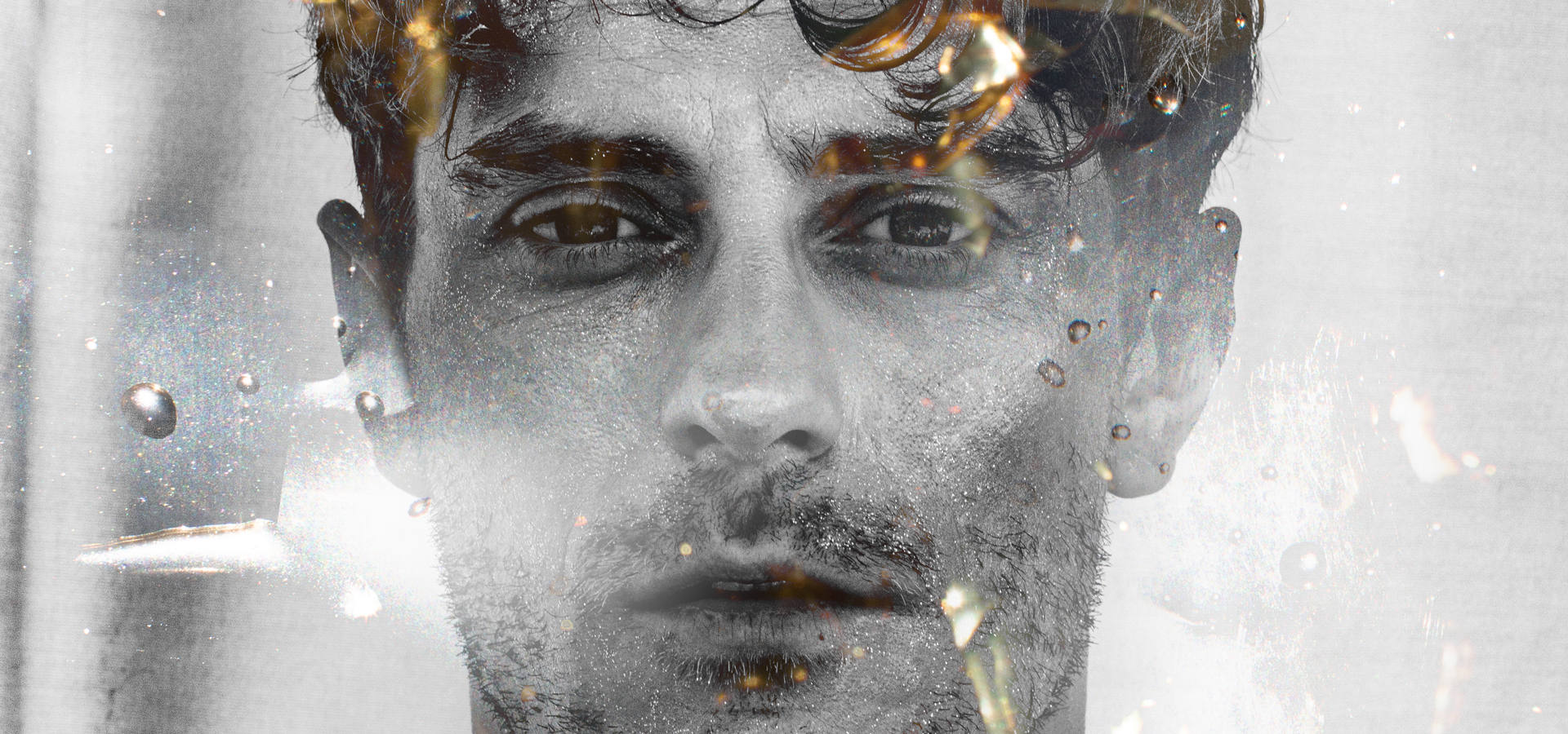 A monochrome photo of Jakub Josef Orlinski’s face, edited with orange sparks as if the image was ignited by flames.