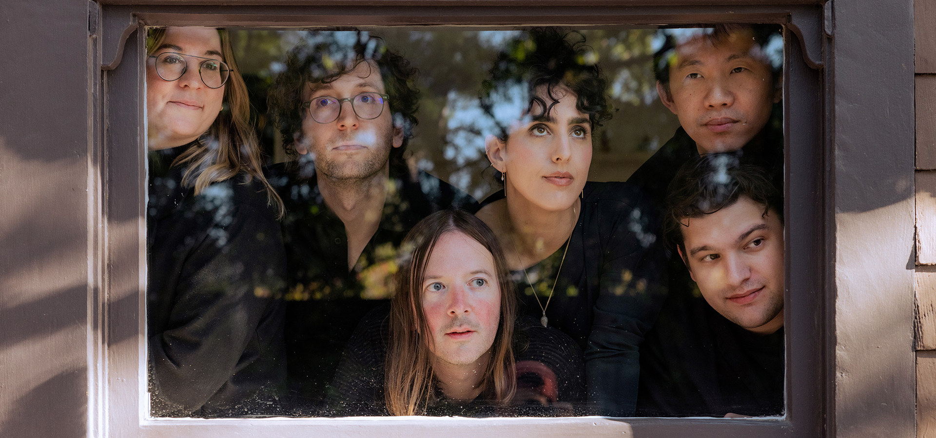 The yMusic Music Group members are arranged framed behind a small window, as they look ponderously through the glass toward the camera.