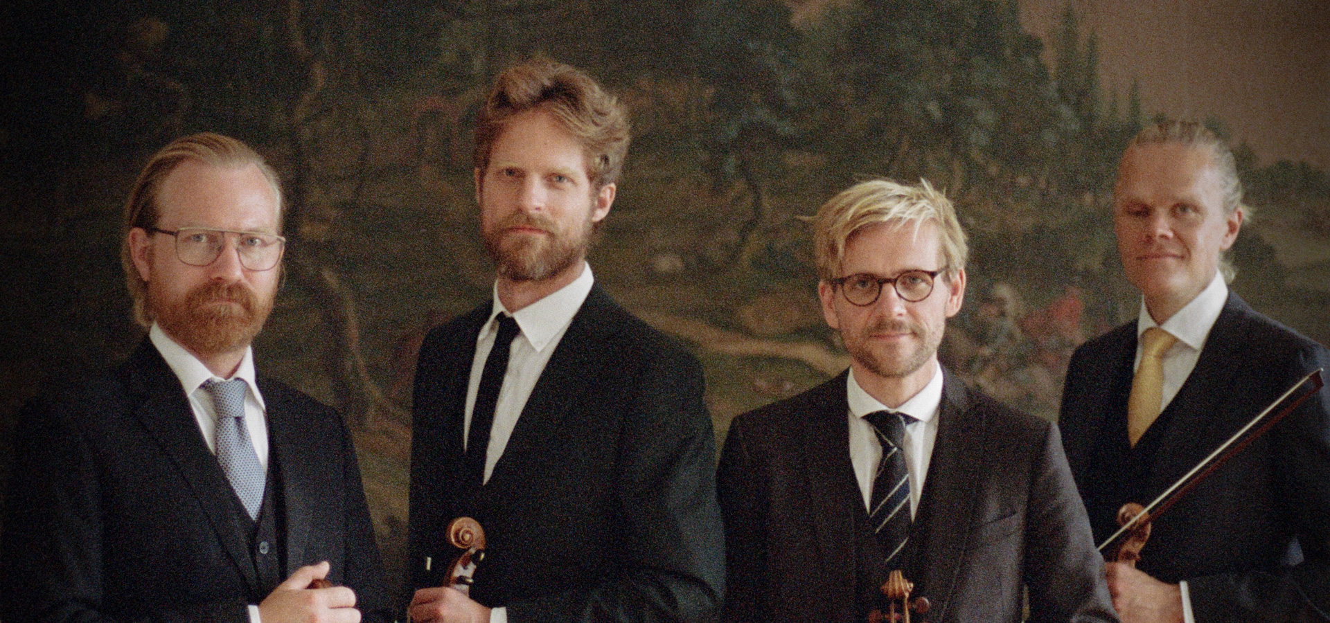 The four men of the Danish String stand next to each other holding their instruments, dressed in suits and ties.