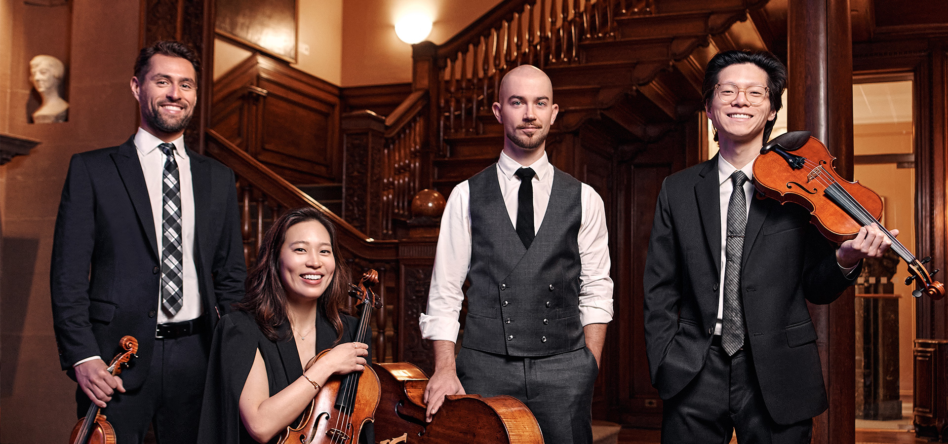 The Dover Quartet, three men and one woman, pose with their instruments in an elegant interior.
