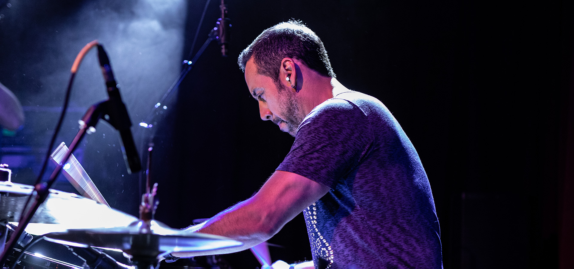 Antonio Sanchez plays the drums on a hazy stage with pink-toned lights amidst his performance of Birdman Live.