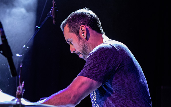 Antonio Sanchez plays the drums on a hazy stage with pink-toned lights amidst his performance of Birdman Live.