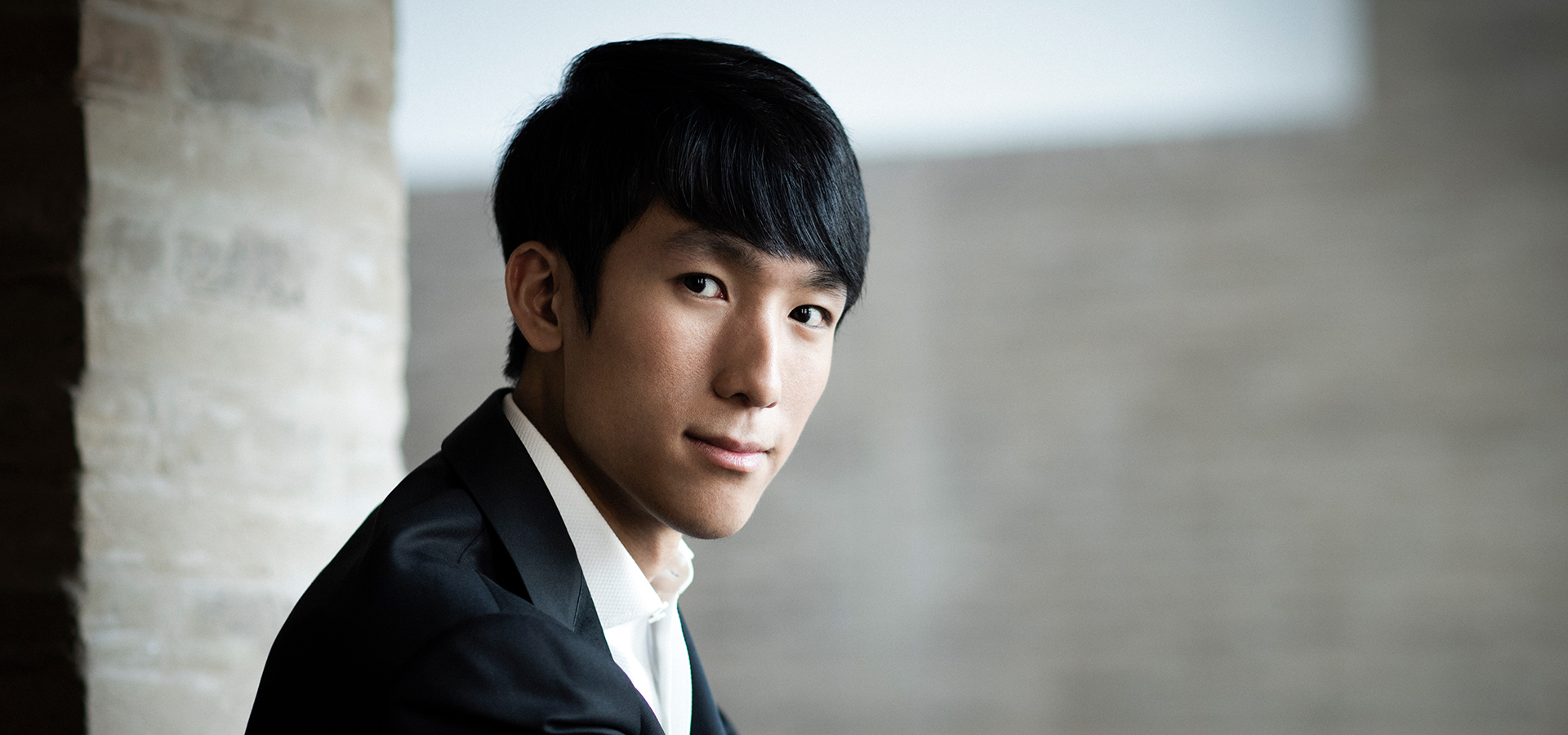 Asian American Pianist Eric Lu looks confidently into the camera wearing a suit and tie.