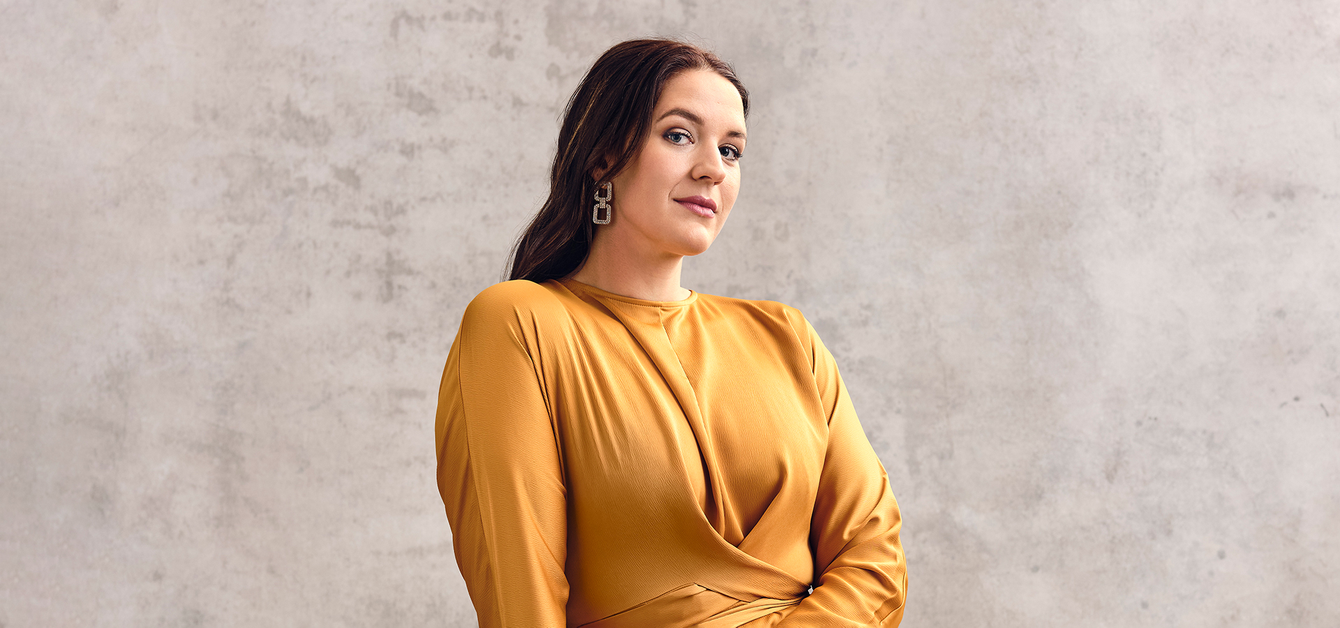 Lise Davidsen, a white woman with brown long hair in a mustard-colored dress, looking into the camera.