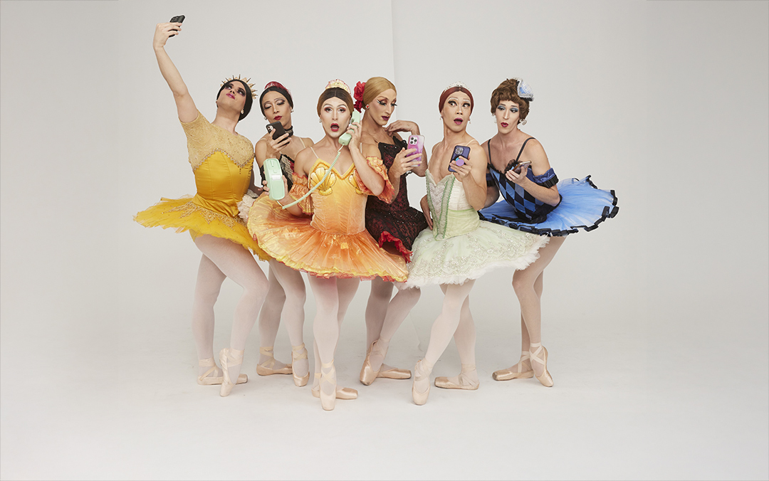 A group photo of Trocks dancers in colorful ballet costumes and pointe shoes comedically posing with varying versions of phones.