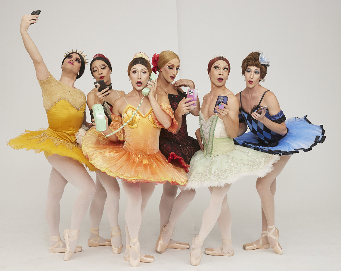 A group photo of Trocks dancers in colorful ballet costumes and pointe shoes comedically posing with varying versions of phones.