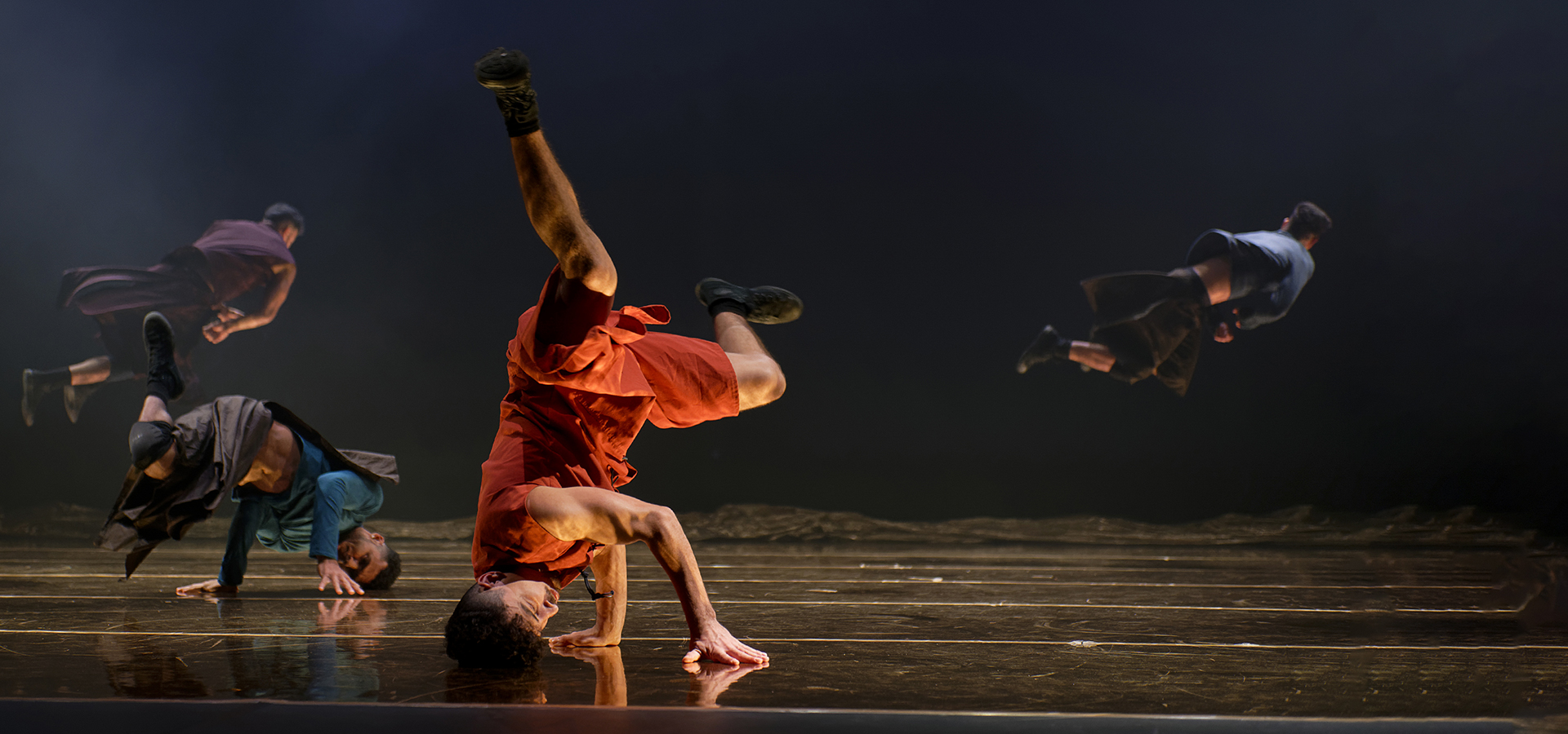 Several dancers of Compagnie Hervé Koubi performing on stage, several on their heads, displaying synchronized movements and colorful costumes.