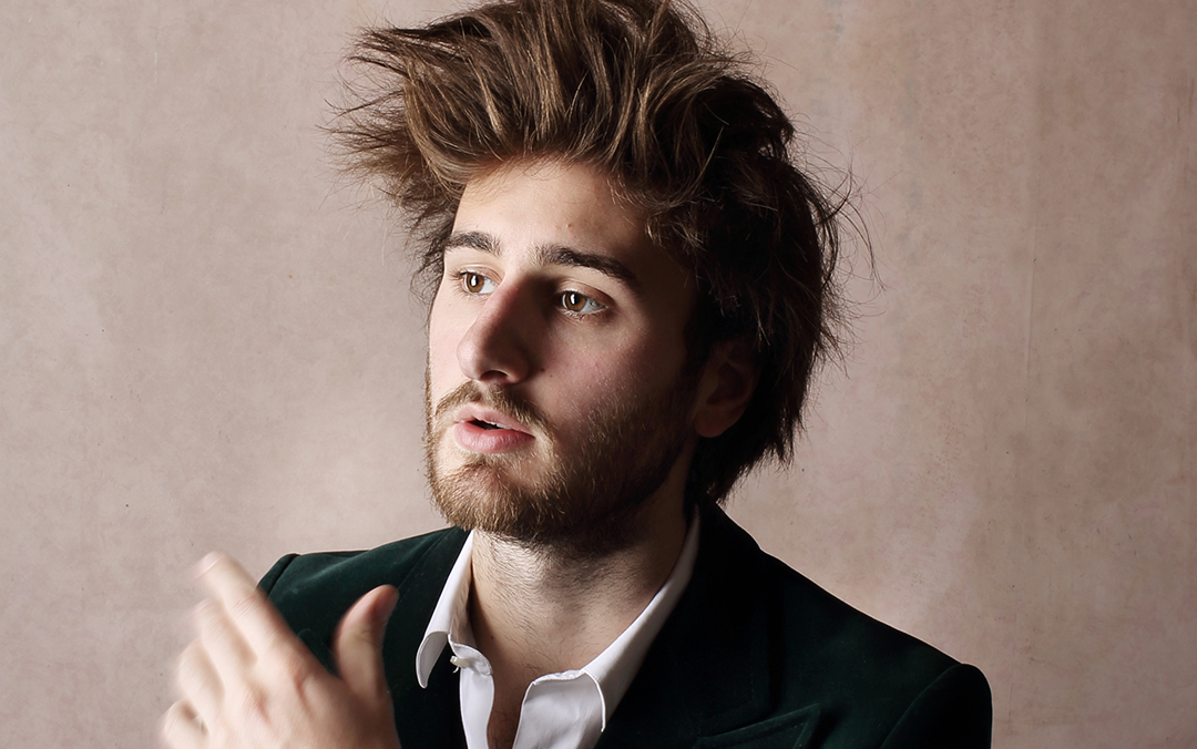 Harpsichordist Jean Rondeau, a white man with tall brown hair and a beard, wearing a dark green jacket, white shirt, and silver bracelets, looks off to the left of the camera.