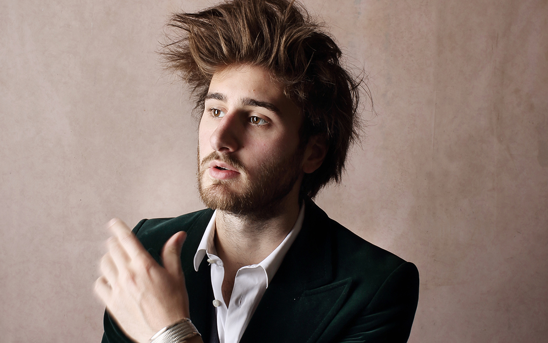 Harpsichordist Jean Rondeau, a white man with tall brown hair and a beard, wearing a dark green jacket, white shirt, and silver bracelets, looks off to the left of the camera.
