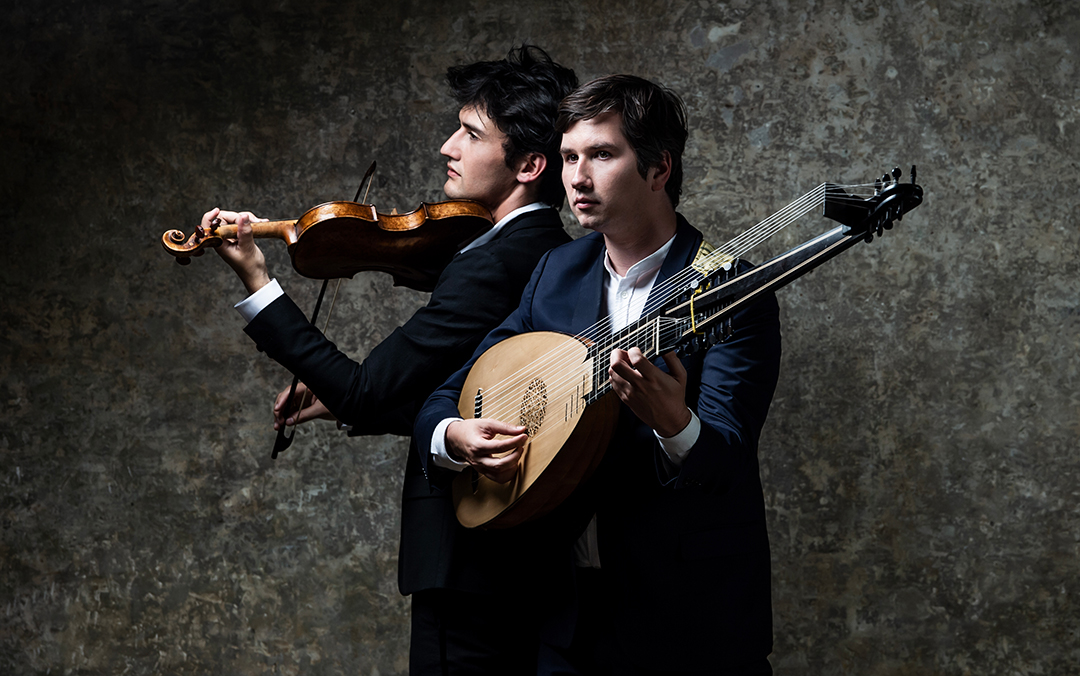 Theotime Langlois de Swarte and Thomas Dunford, two white men in suits, one holding a violin and the other a lute, stand together, showcasing their musical instruments.