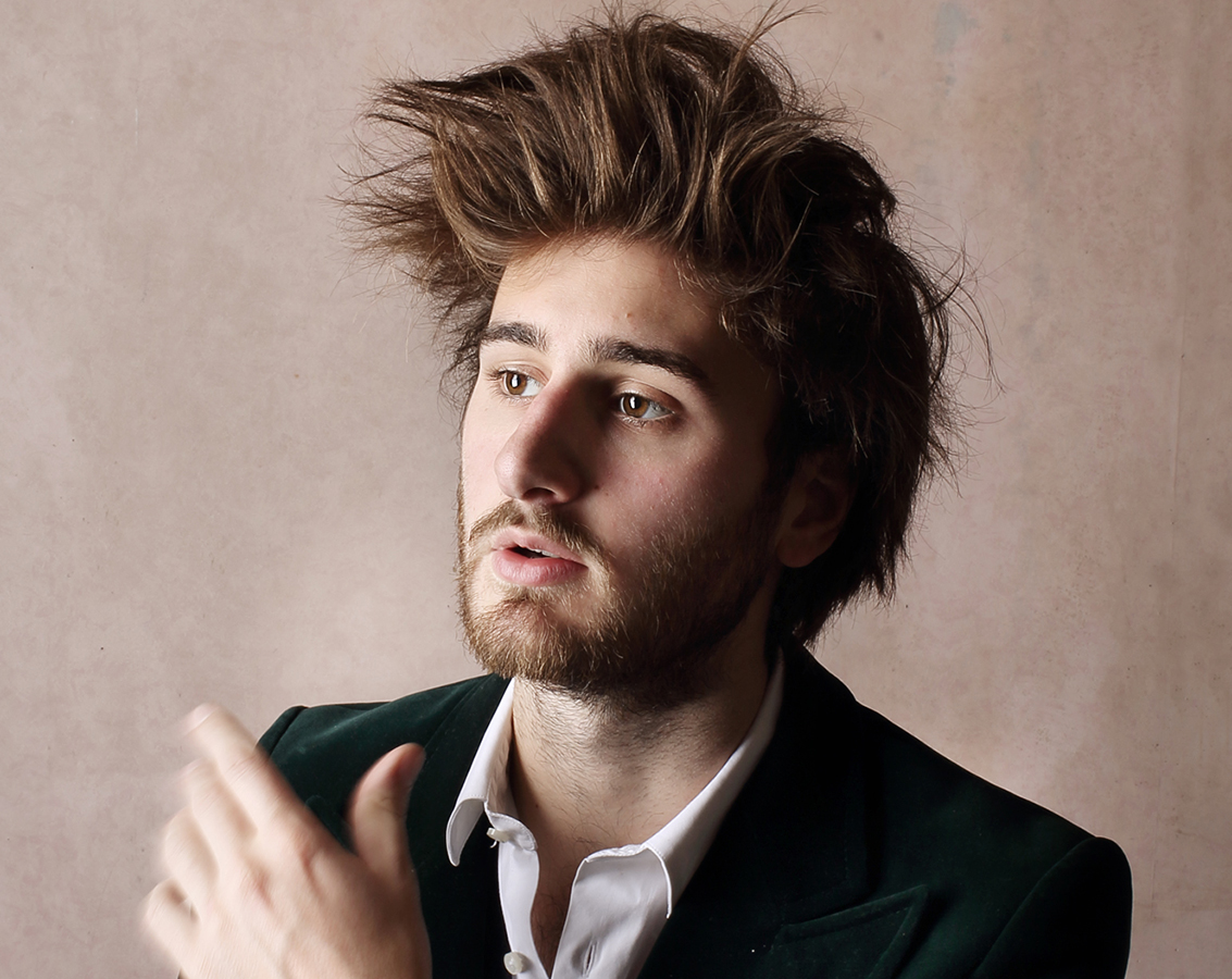 Harpsichordist Jean Rondeau, a white man with tall brown hair and a beard, wearing a dark green jacket, white shirt, and silver bracelets, looks off to the left of the camera.