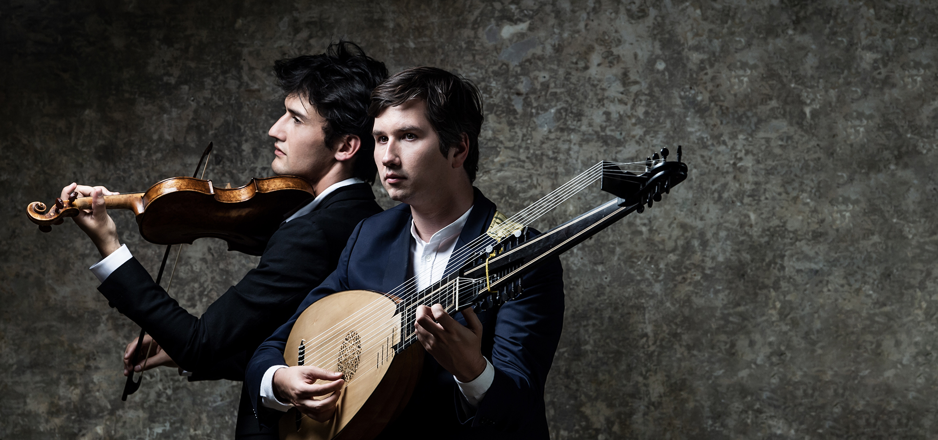 Theotime Langlois de Swarte and Thomas Dunford, two white men in suits, one holding a violin and the other a lute, stand together, showcasing their musical instruments.