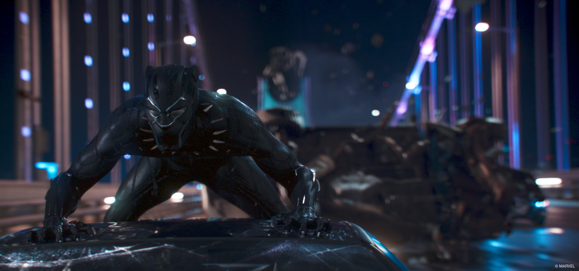 A scene from Marvel Studio's film Black Panther, where the title character crouches on top of a moving car on a bridge.