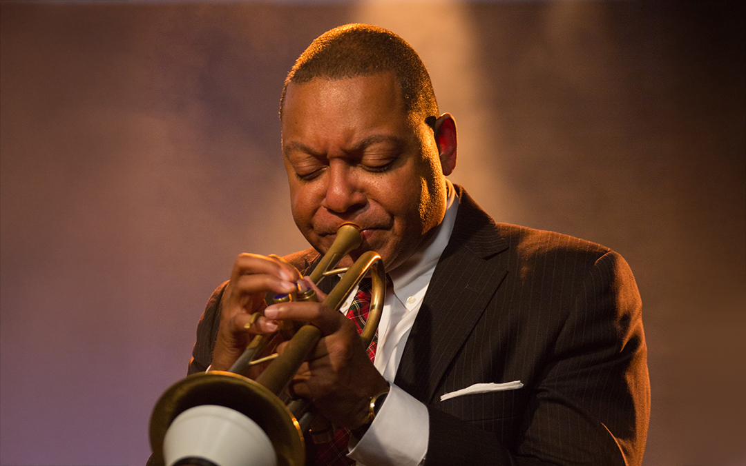 Famed trumpeter Wynton Marsalis of Jazz at Lincoln Center Orchestra, a black man in a dark suit and red tie playing his instrument.