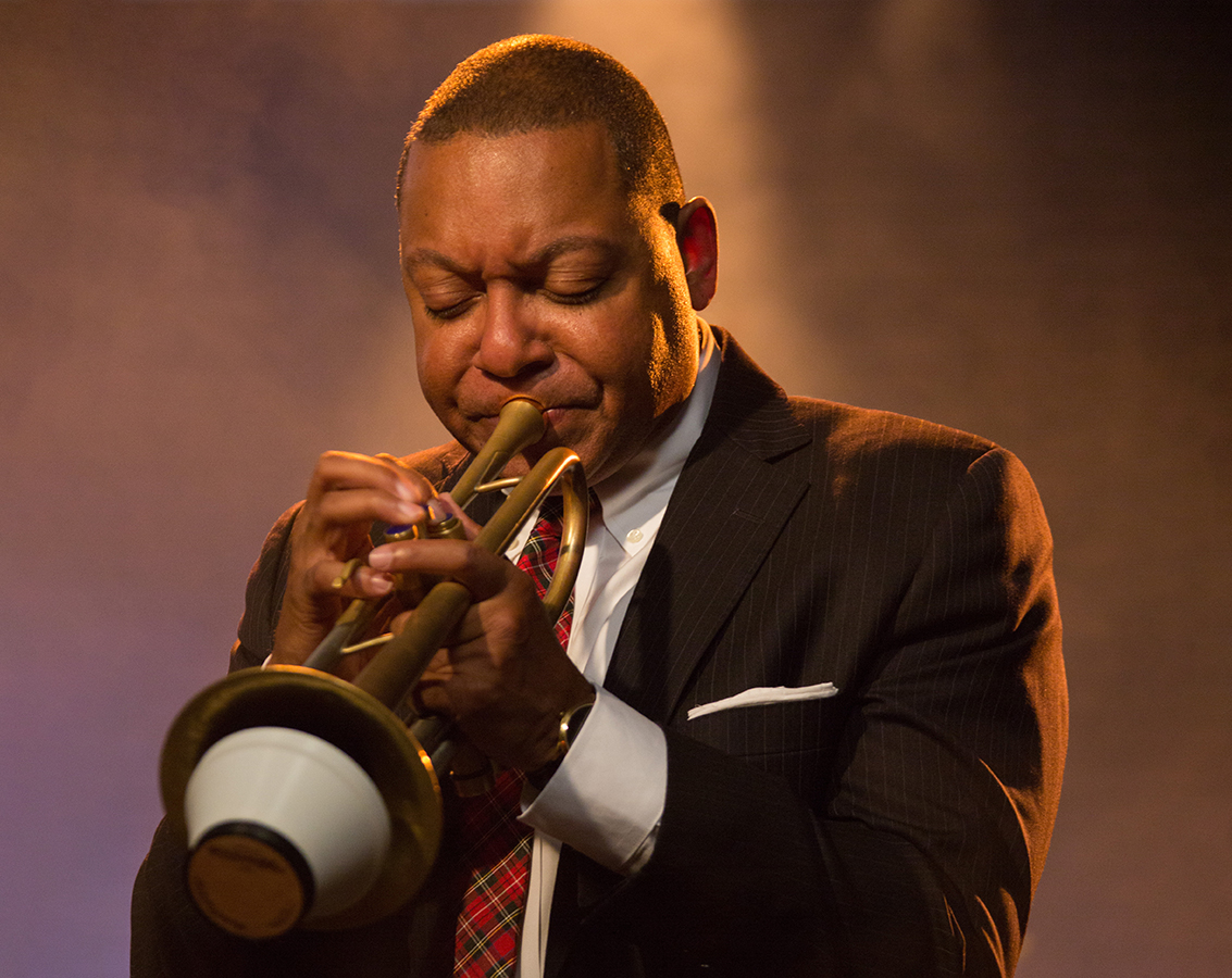 Famed trumpeter Wynton Marsalis of Jazz at Lincoln Center Orchestra, a black man in a dark suit and red tie playing his instrument.