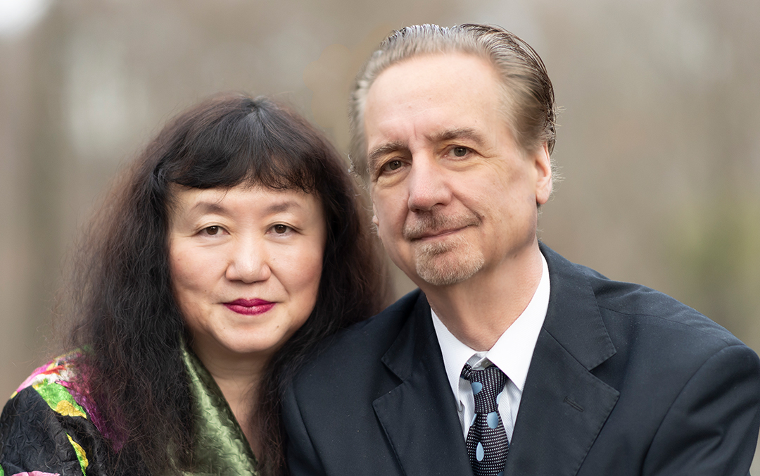 Veteran musicians and married couple David Finckel, a white man, and Wu Han, an Asian woman, pose together in an outdoor setting.