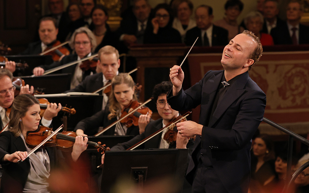 Members of the Vienna Philharmonic conducted by Yannick Nézet-Séguin, a white man in a dark suit, with an audience watching on.