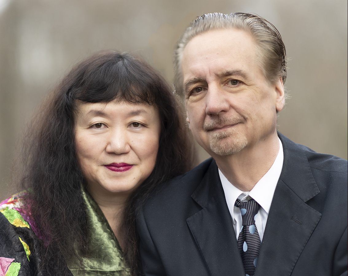 Veteran musicians and married couple David Finckel, a white man, and Wu Han, an Asian woman, pose together in an outdoor setting.