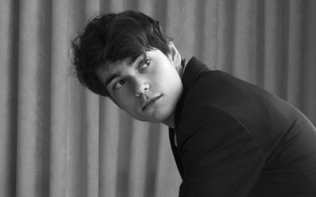 Pianist Tom Borrow, a white man in a dark suit, leans forward from a seated position in this black and white photo.