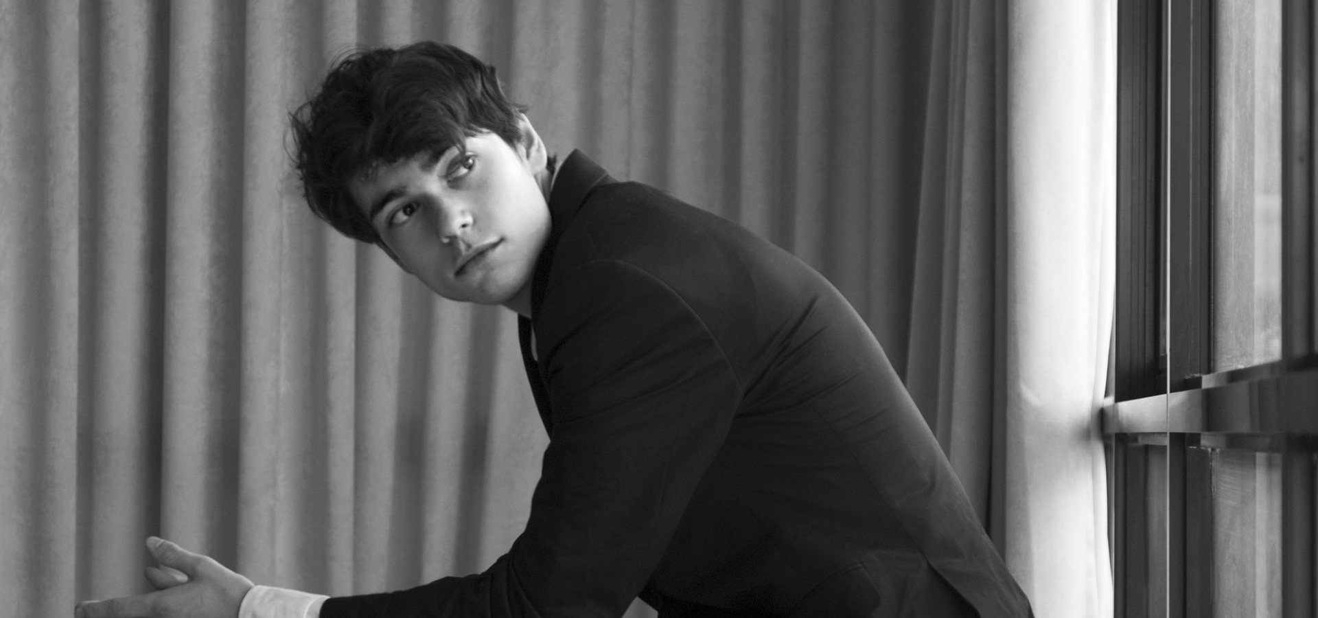 Pianist Tom Borrow, a white man in a dark suit, leans forward from a seated position in this black and white photo.