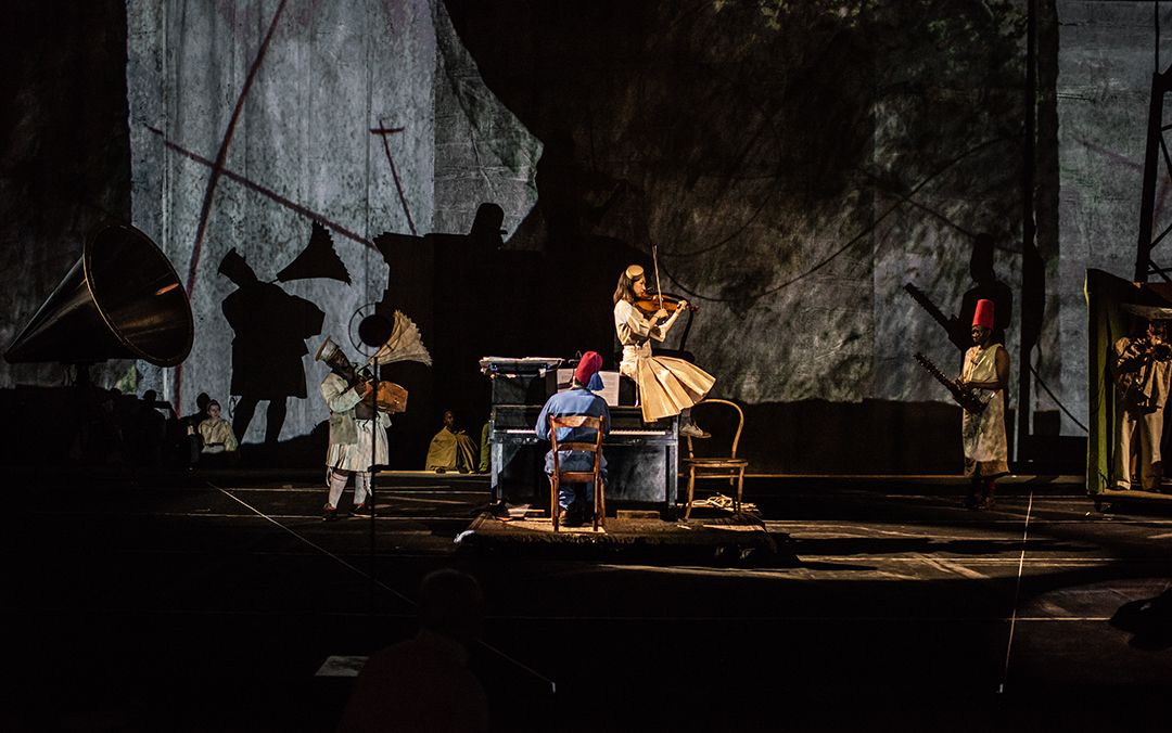 A photo of a scene from William Kentridge's The Head and The Load, the actors playing several instruments against a multimedia backdrop.