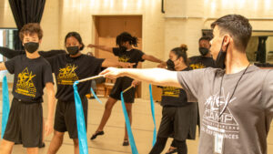 Aileycamp members learn choreography for a ribbon dance, each holding a stick with long blue ribbons attached