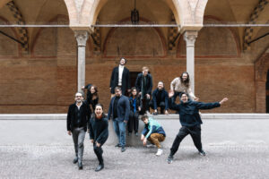 The Il Pomo Doro group poses against an a historical building with large arches, each making playful gestures.