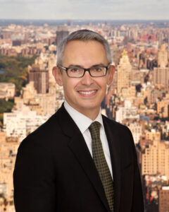 Executive Director Bennett Rink wearing glasses, a suit, and tie against a cityscape background.