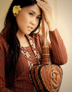 Peni Candra Rini holding her instrument wearing a striped, traditional outfit with a flower in her hair.