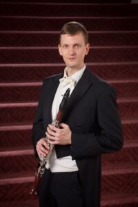Carey Bell, a clarinetist, stands in front of a red staircase holding his clarinet.