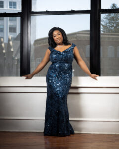 Michelle Cann wears a sparkling navy blue dress and poses against a window.