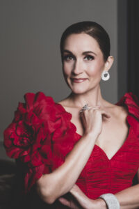 Artist Erin Morley smiles towards the camera in a vibrant red dress and silver earrings.