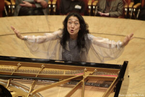 Mitsuko Uchida in the middle of conducting, passionately extending her arms.