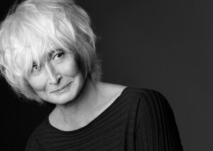 A black and white portrait image of choreographer Twyla Tharp, who leans to the left side of the frame while smiling softly.