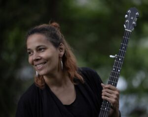 Rhiannon Giddens, a tan woman with wavy brown and orange hair half tied up into a bun, looks at something off to her side