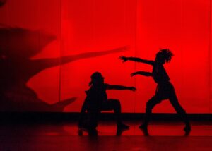 Two dancers perform on a stage illuminated with bright red lights.