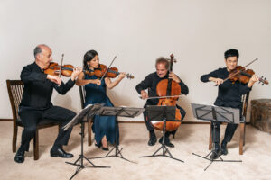The Takacs Quartet play in a carpeted room in front of a white wall.