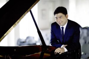 Behzod Abduraimov sitting and smiling at a grand piano.