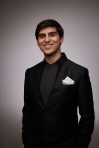 Evren Ozel smiles wearing a nice black suit with a white pocket square.