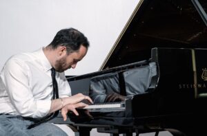 Igor Levit looking at the keys of a shiny grand piano.