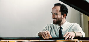 Igor Levit smiling and sitting on a piano bench.