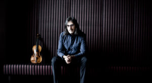 Leonidas Kavakos sits with his hands on his knees next to his violin.